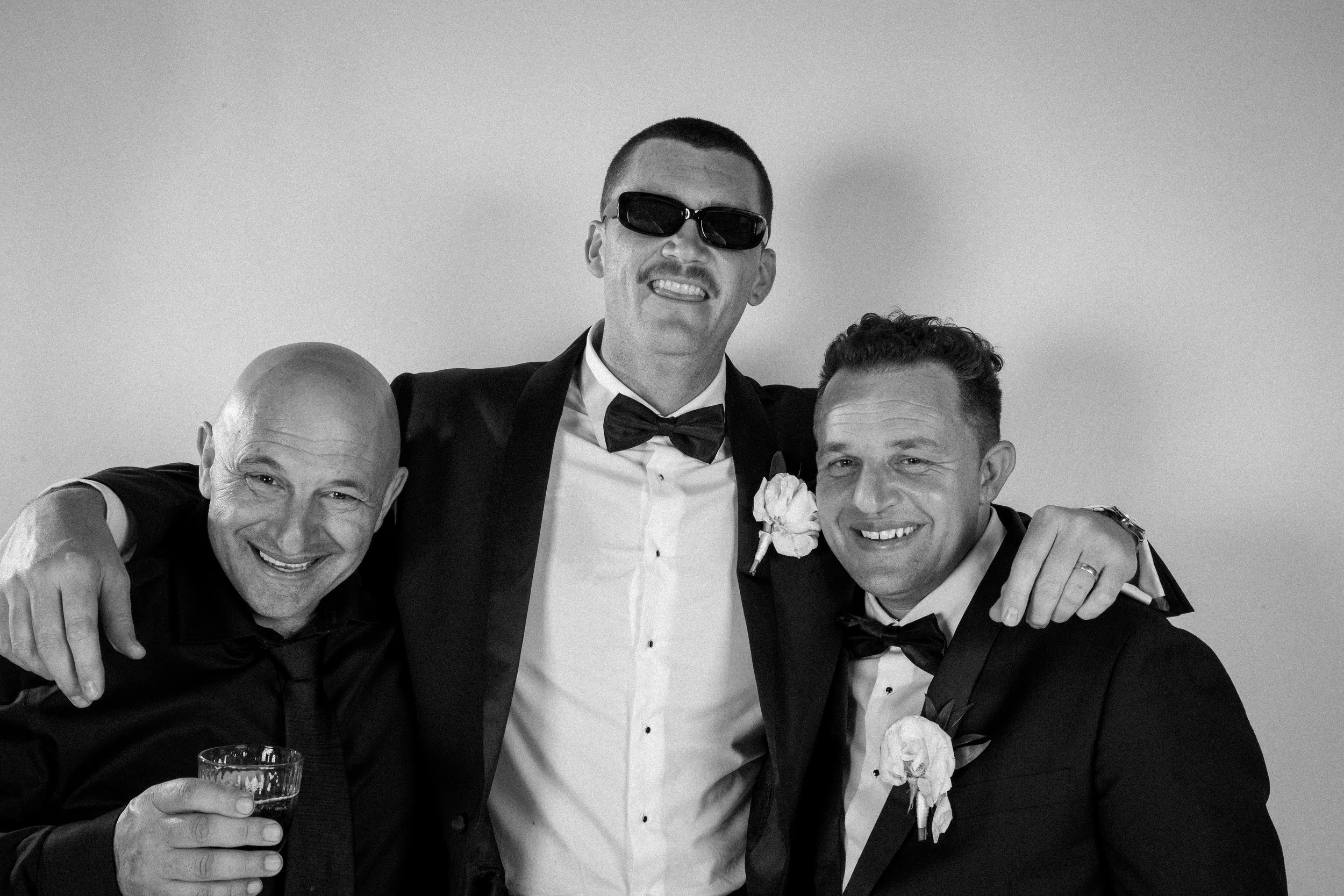 Three men in suits laughing and posing together in a high-end glam studio photography setting.