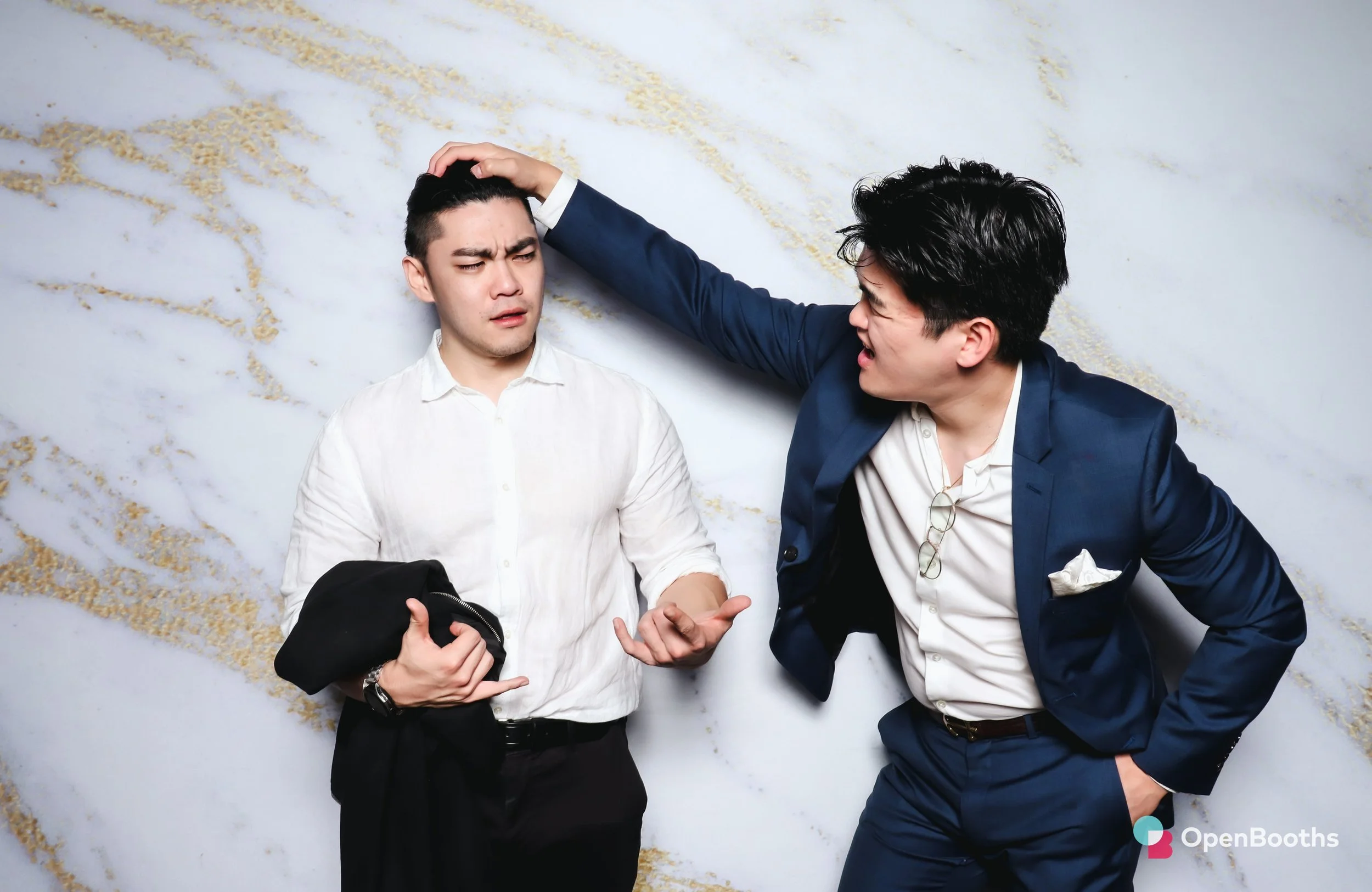 Two people pose in an Open Booths photo booth with a white and gold marble print backdrop