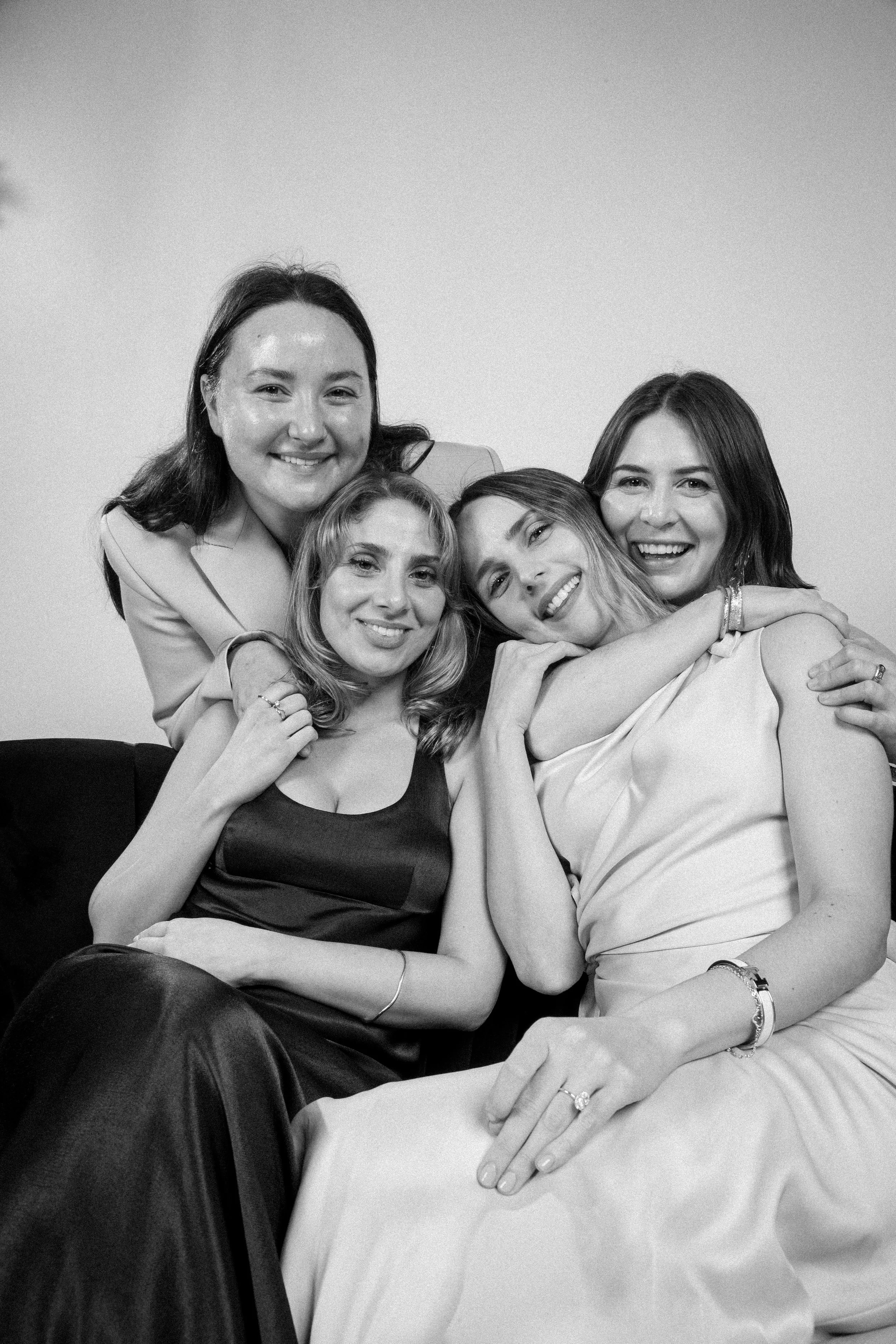 Group of four women smiling and hugging inside a glam photo booth with soft studio lighting