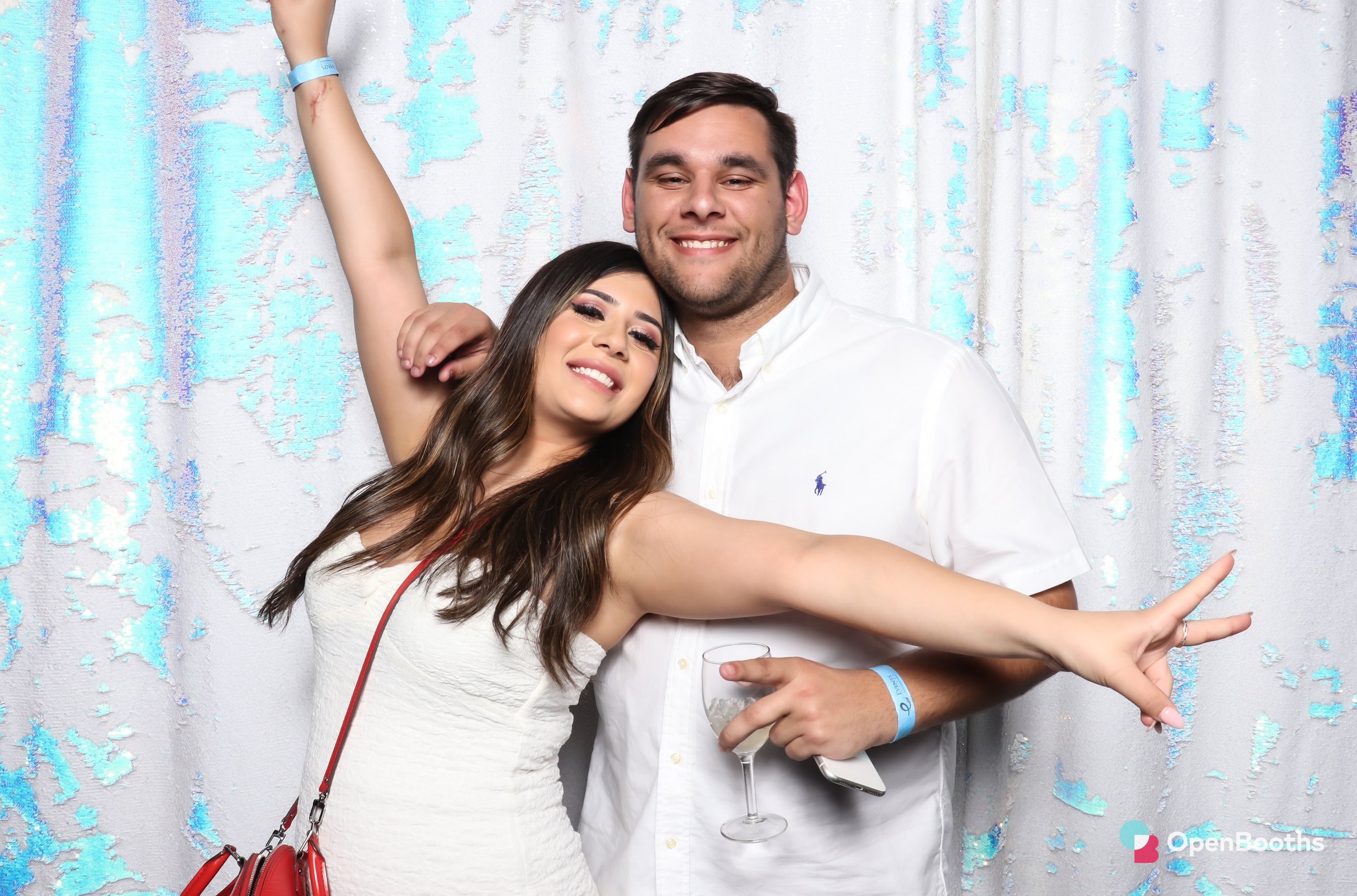 Two people pose in an Open Booths photo booth with a majestic mermaid sequin backdrop