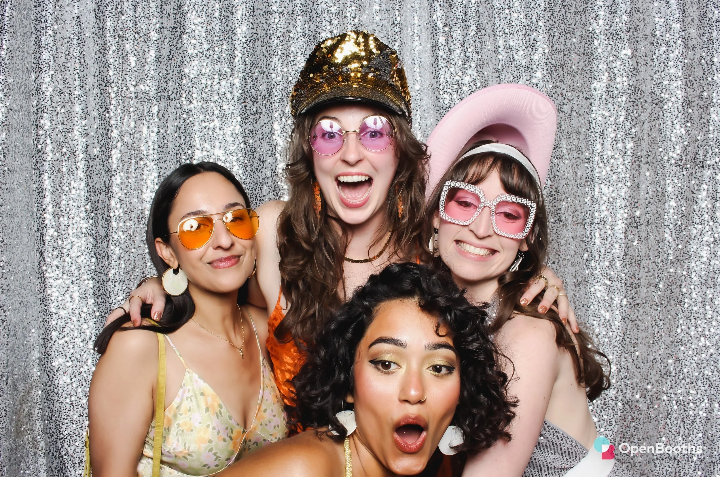 Four women pose in an Open Booths photo booth in front of  a sparkly silver sequin backdrop