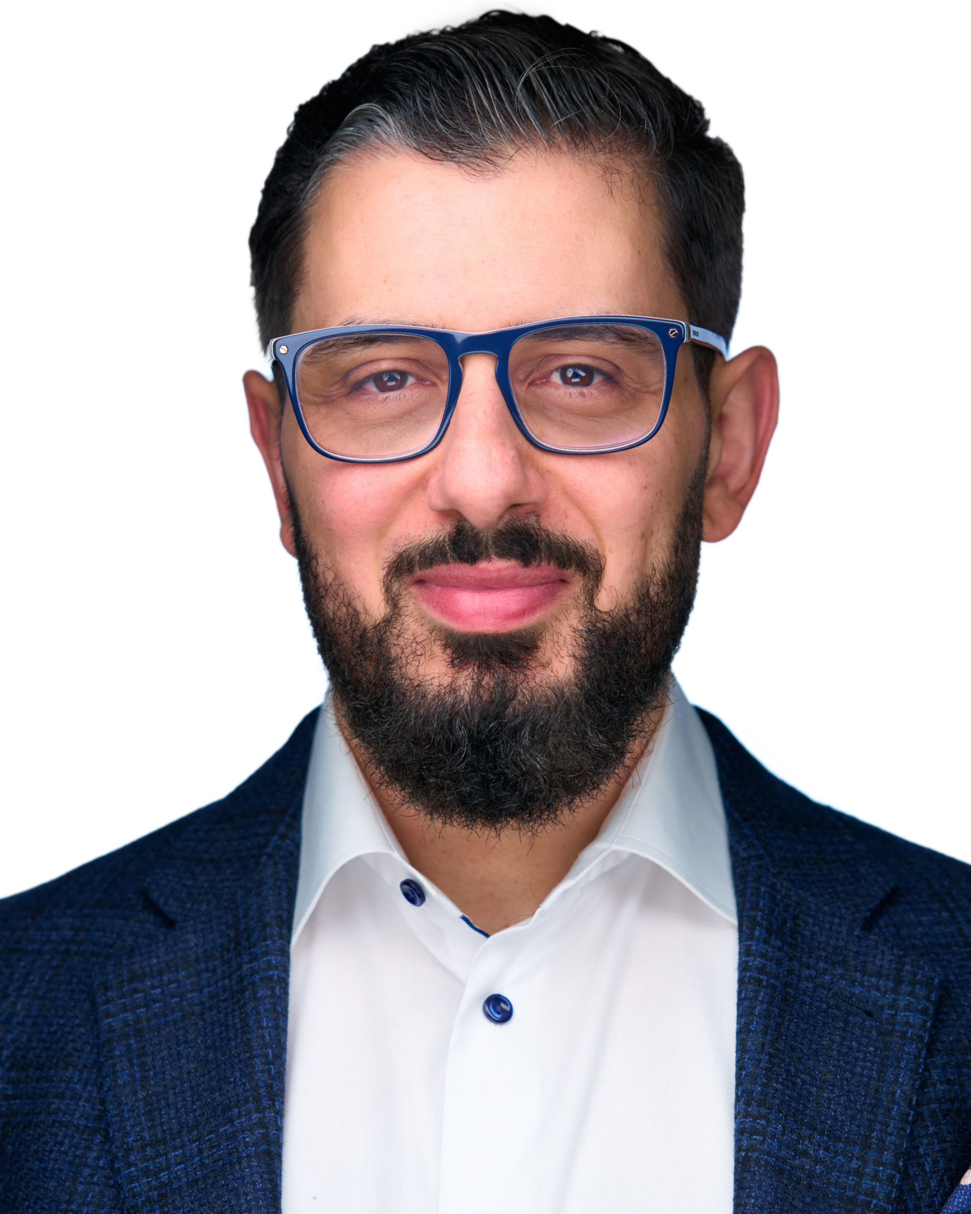 A man with dark hair, brown eyes, and a beard, wearing blue glasses, a white shirt, and a dark blue blazer, smiling against a white background.