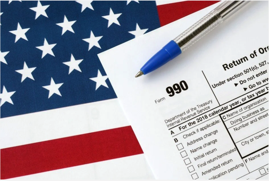 An IRS Form 990 for the 2018 calendar year on a paper with an American flag background and a blue pen placed on top.