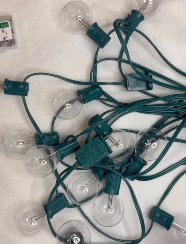 String of clear light bulbs with blue sockets and cords, tangled on a surface.