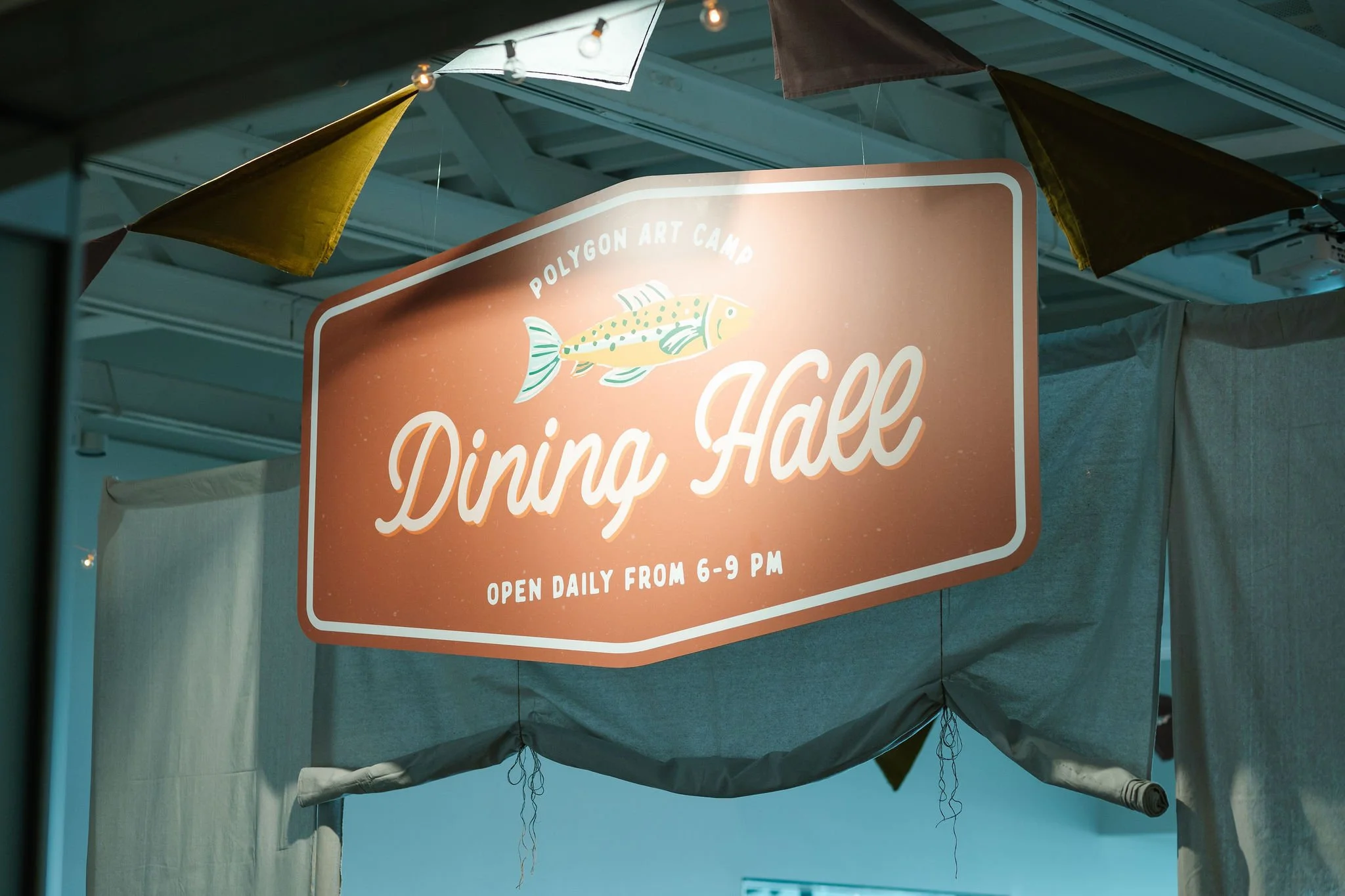 Lighted sign for Polygon Art Camp titled 'Dining Hall' with a fish illustration, indicating hours from 6 to 9 PM, hanging inside a tent or canopy.