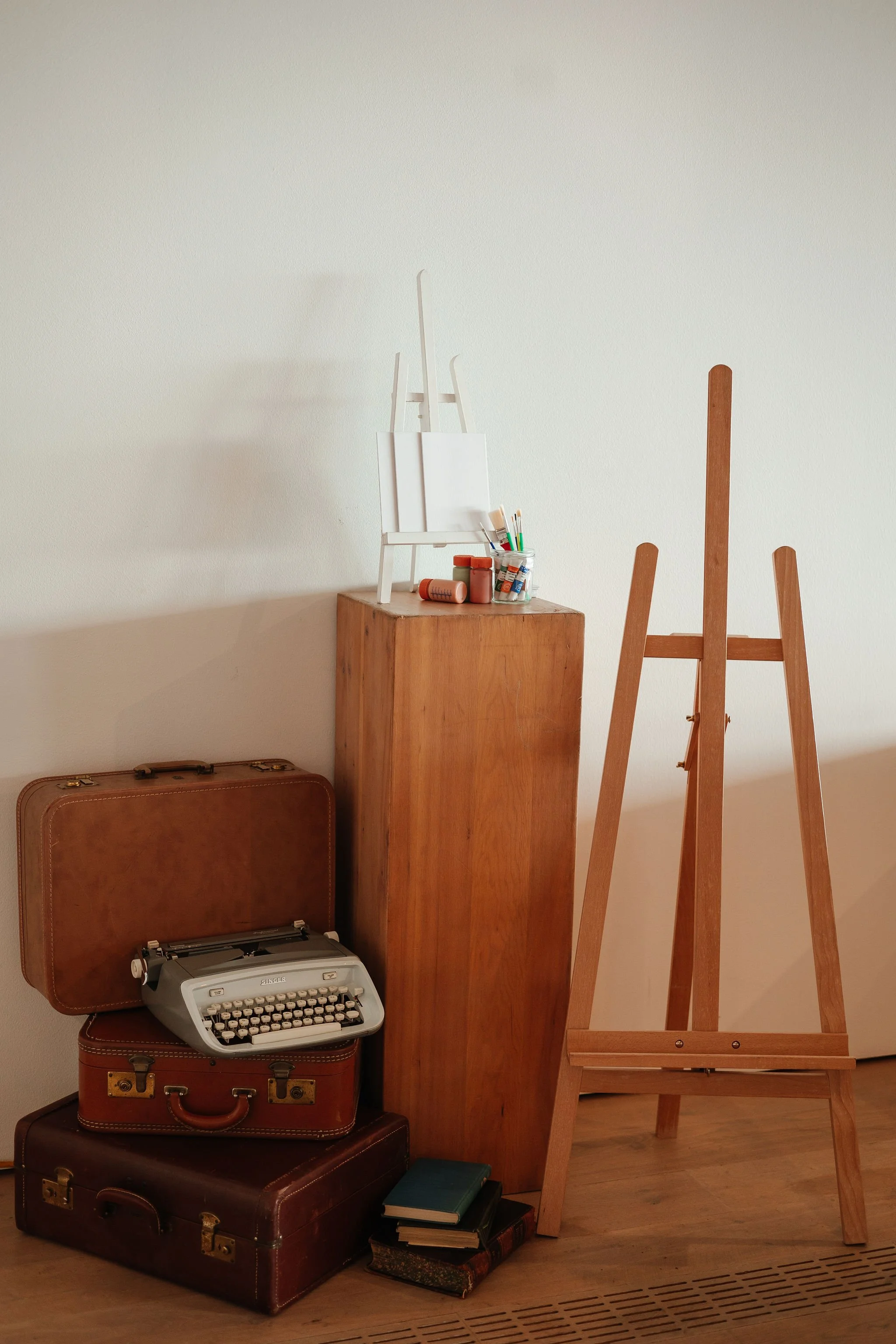An art easel, a vintage typewriter, books, a wooden pedestal with art supplies, and a blank canvas in an art studio