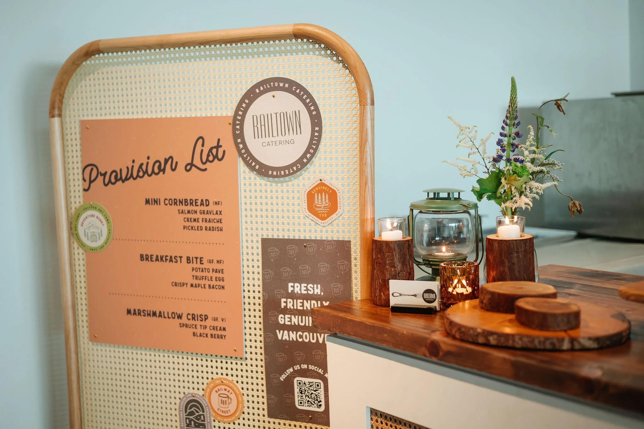 Catering menu board with provision list, candles, and flowers on a wooden counter in a cafe.