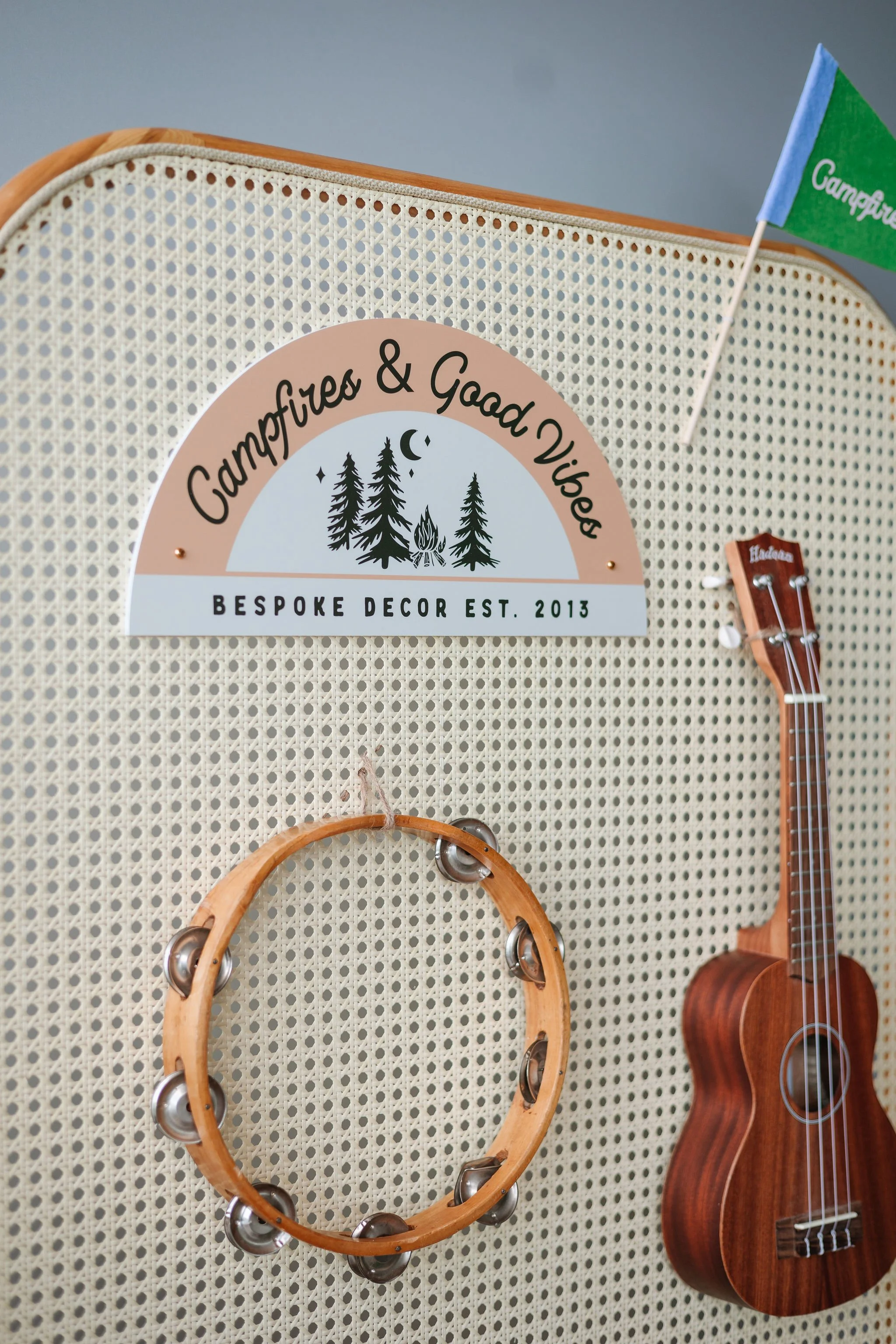 A display board with a sign that reads "Campfires & Good Vibes, Bespoke Decor Est. 2013," a small green flag, a tambourine, and a ukulele.