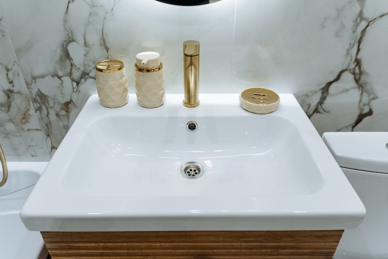 bathroom remodel interior design with gold brushed bathroom sink faucet, white sink, and marble walls