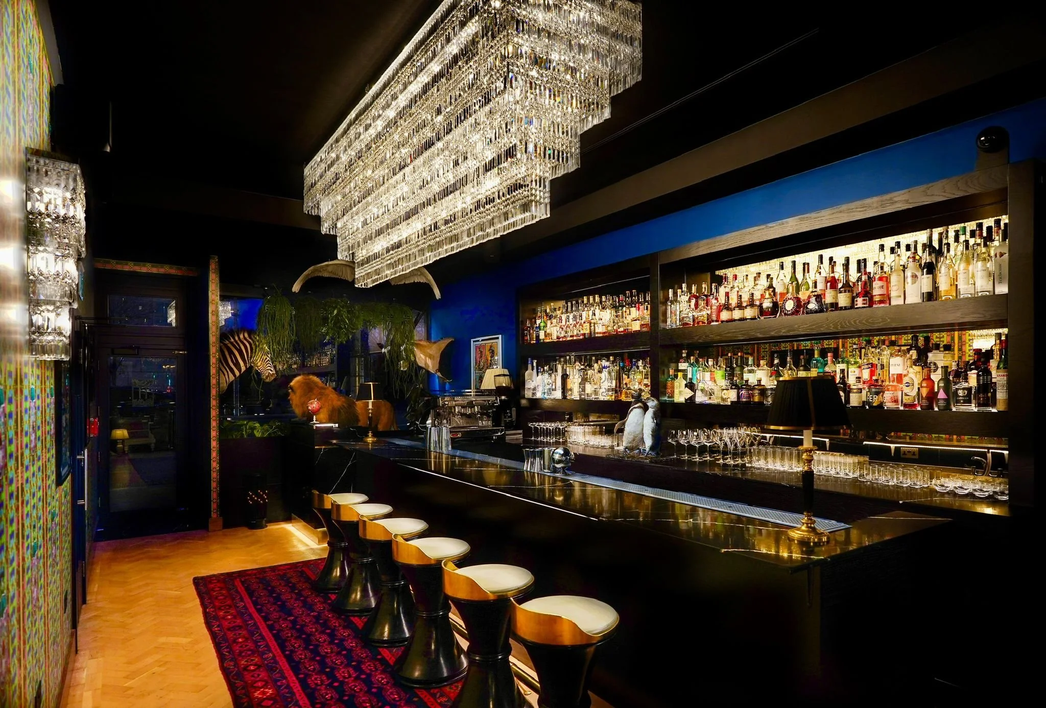 Hux Bar with a crystal chandelier, blue walls and gold bar stools