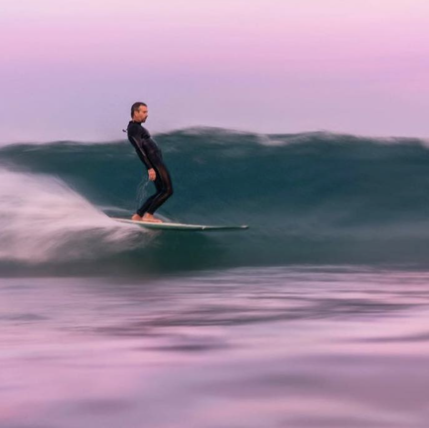 A person surfing on a wave in the ocean during sunset or sunrise.