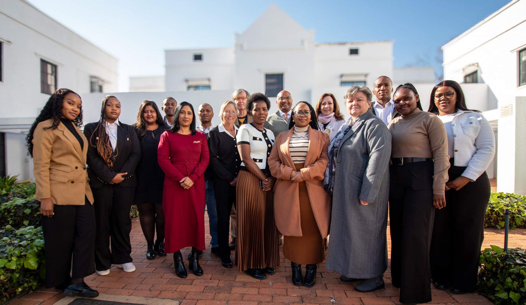 Group of diverse professionals in the Insurance Guarantee industry standing together outdoors in front of white buildings, dressed in business attire.