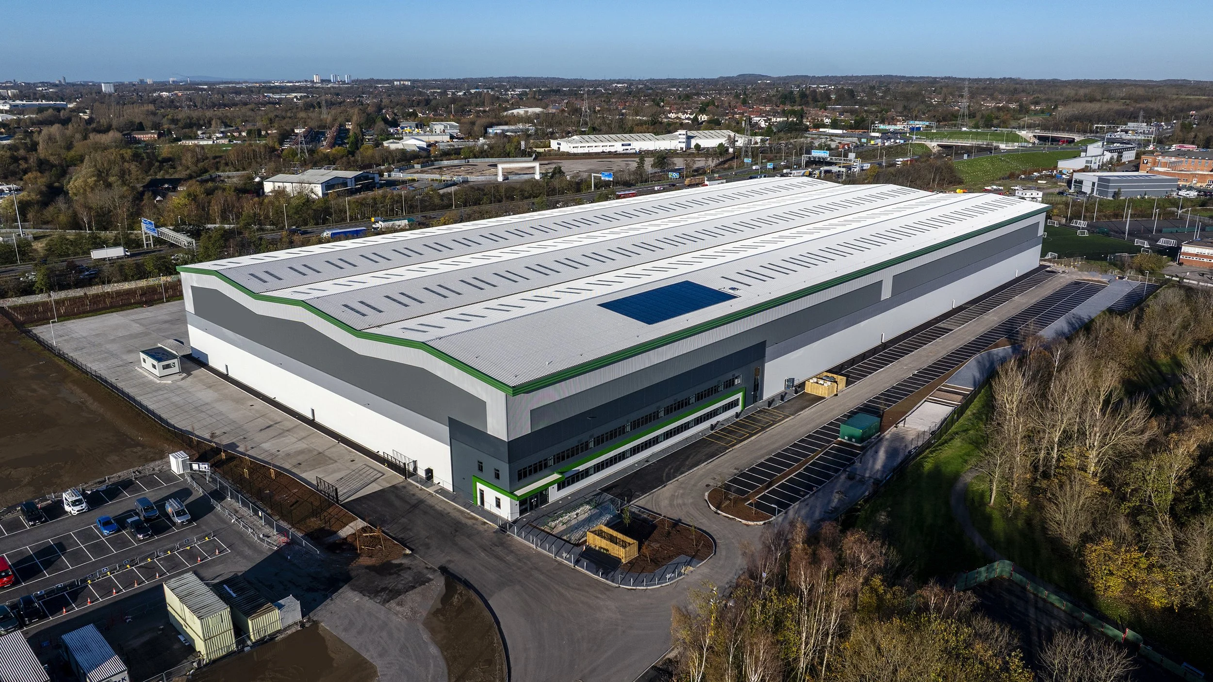 A large, modern warehouse building with a gray and white exterior, surrounded by parking lots and greenery, in an industrial area.