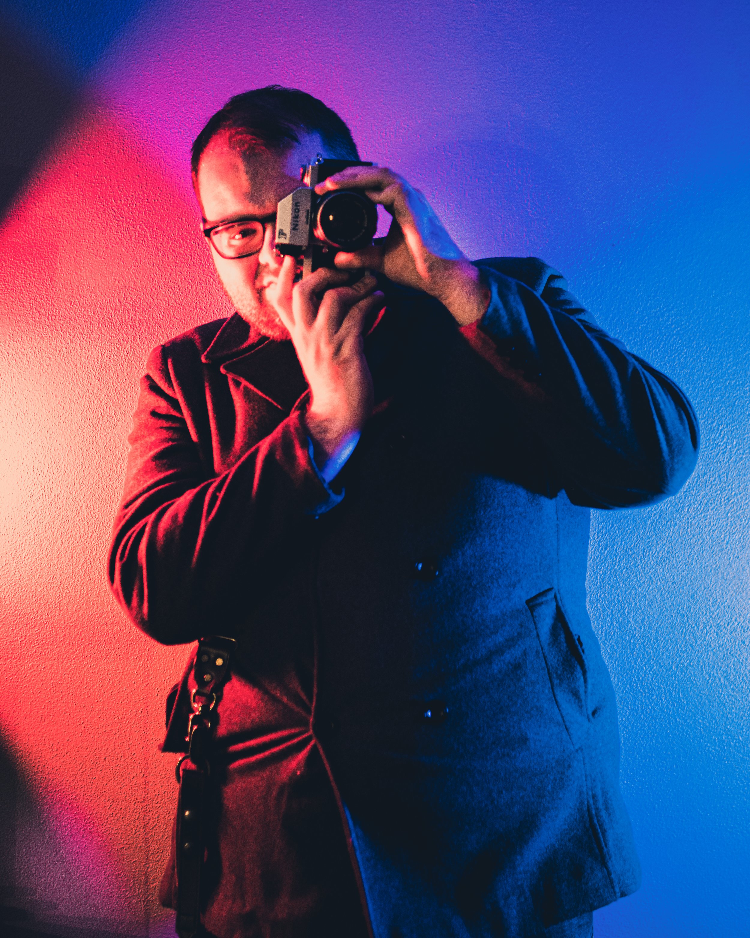 Picture of Jake Perusich holding a camera in front of a moody light
