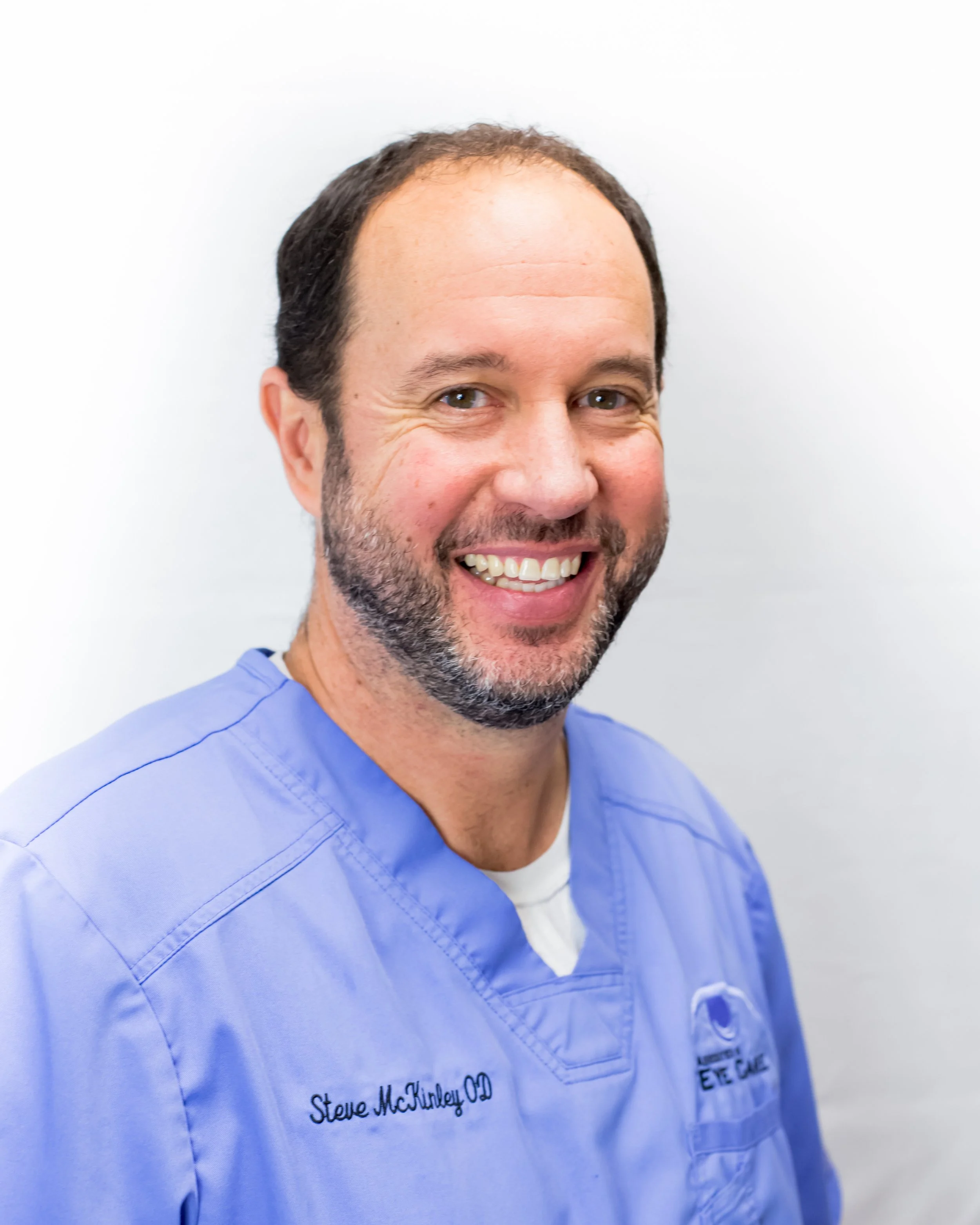 Smiling Stephen McKinley, OD, in Whitley City, KY, in light blue scrubs with embroidered name "Steve McKinley OD."