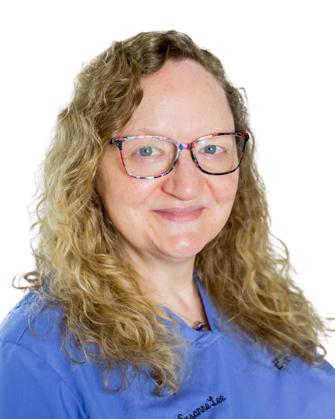 Person with curly hair wearing glasses and a blue top, smiling against a white background.