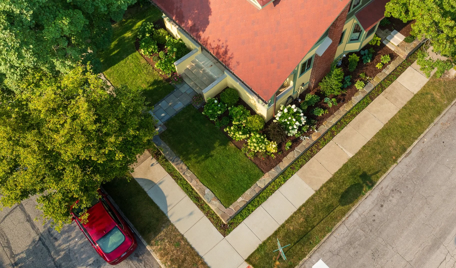 Aerial view of the finished front corner with fieldstone retaining walls, bluestone walks and layered plantings resolving the grade change