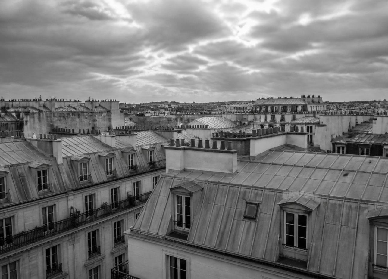 Toits de zinc et souches de cheminées d'immeubles haussmanniens à Paris sous un ciel nuageux