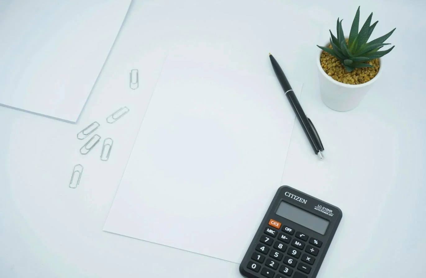 Calculatrice, stylo et feuille blanche sur un bureau, pour simuler la fiscalité d'une location meublée