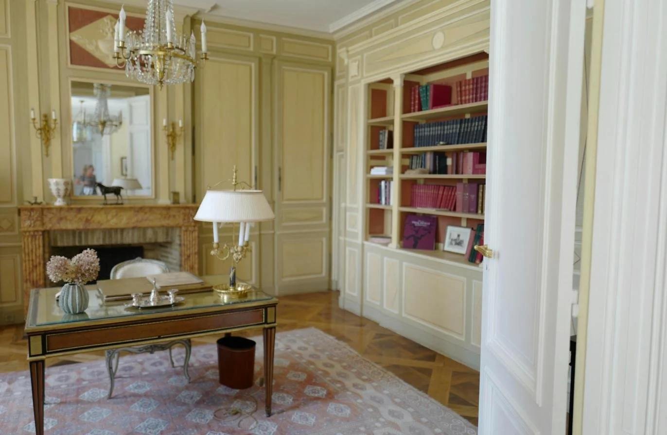 Bureau d'un appartement parisien meublé avec boiseries, cheminée en marbre et bibliothèque, illustrant la location meublée LMNP