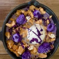 A bowl of ice cream topped with purple grapes, caramel cubes, and purple syrup.
