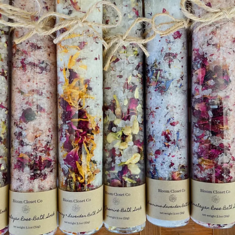 Five bath salts or similar products rolled in decorative paper with floral and abstract patterns, arranged in a row.