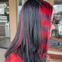 Woman with long black hair and red highlights, wearing a red top, in a salon or shop interior