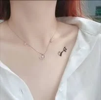 Close-up of a person's collarbone with a small star tattoo and layered necklaces, wearing a white shirt.