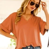 Woman wearing sunglasses, casual orange t-shirt, and blue jeans, posing outdoors.