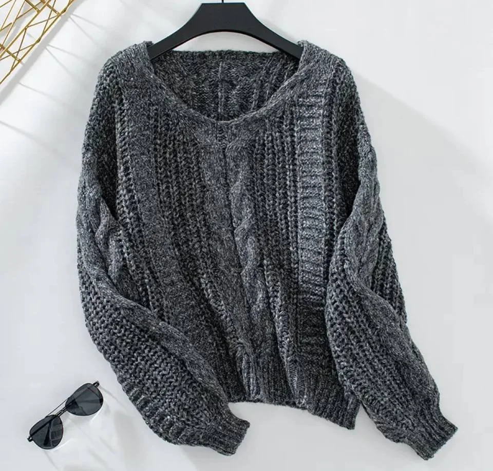 A gray, cable-knit sweater hanging on a black hanger on a white background with a pair of black sunglasses placed nearby.