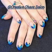 Close-up of hands with blue and black tie-dye style nail polish and decorated nails.