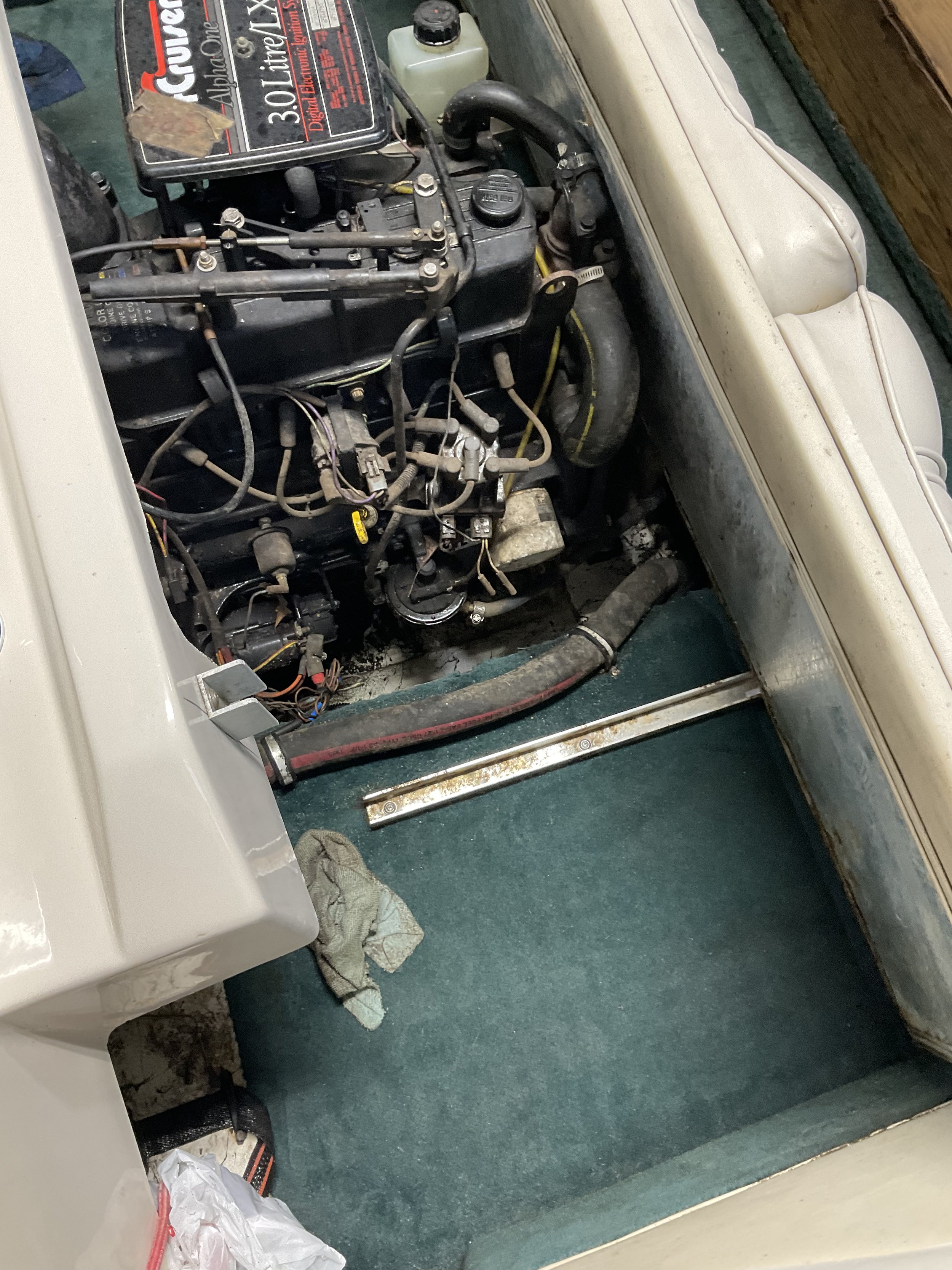 Inboard boat engine compartment with a 3.0 liter engine, wiring, hoses, and mechanical components visible on a carpeted surface.