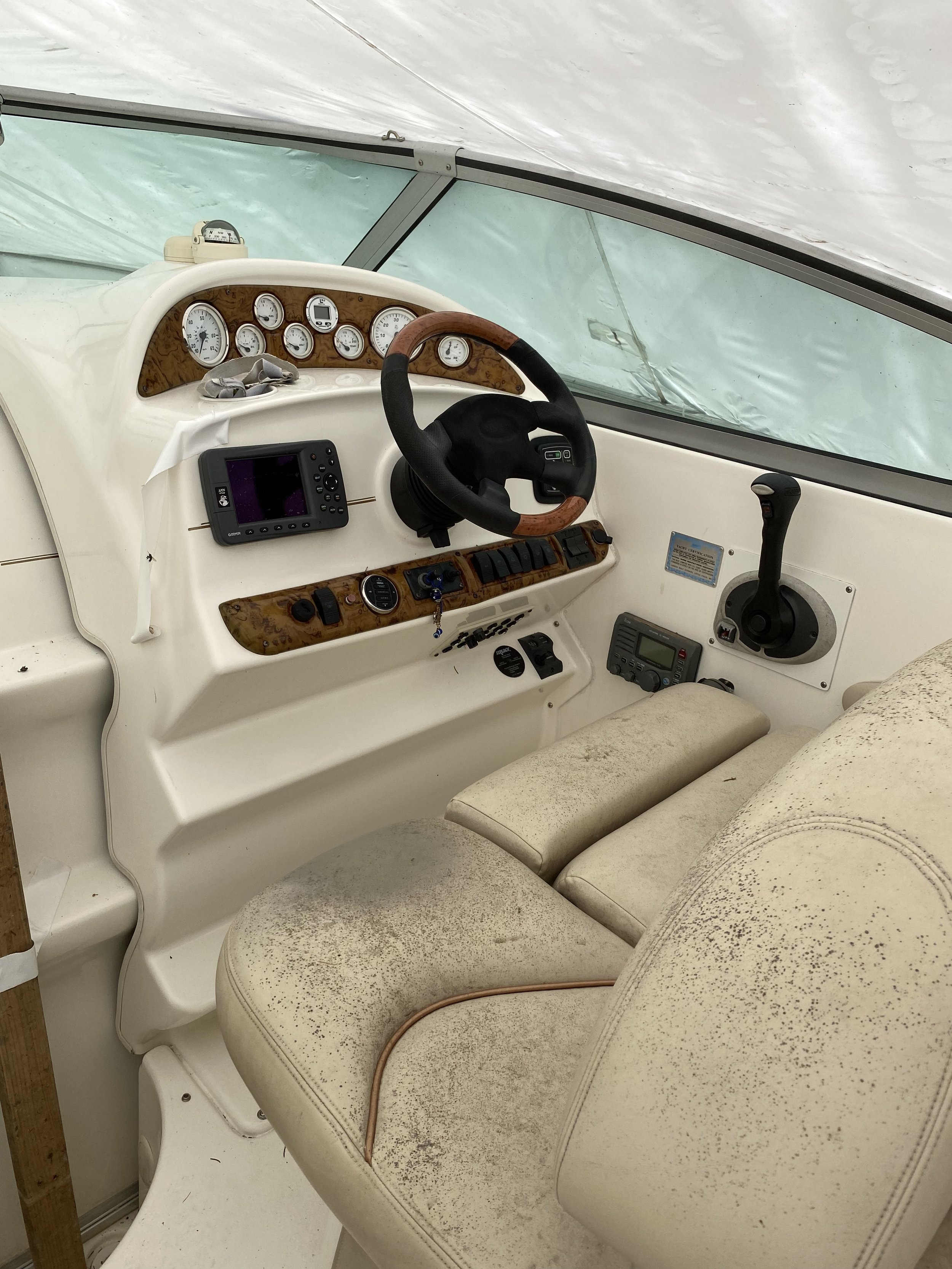 Boat cockpit interior with steering wheel, gauges, and worn seat.