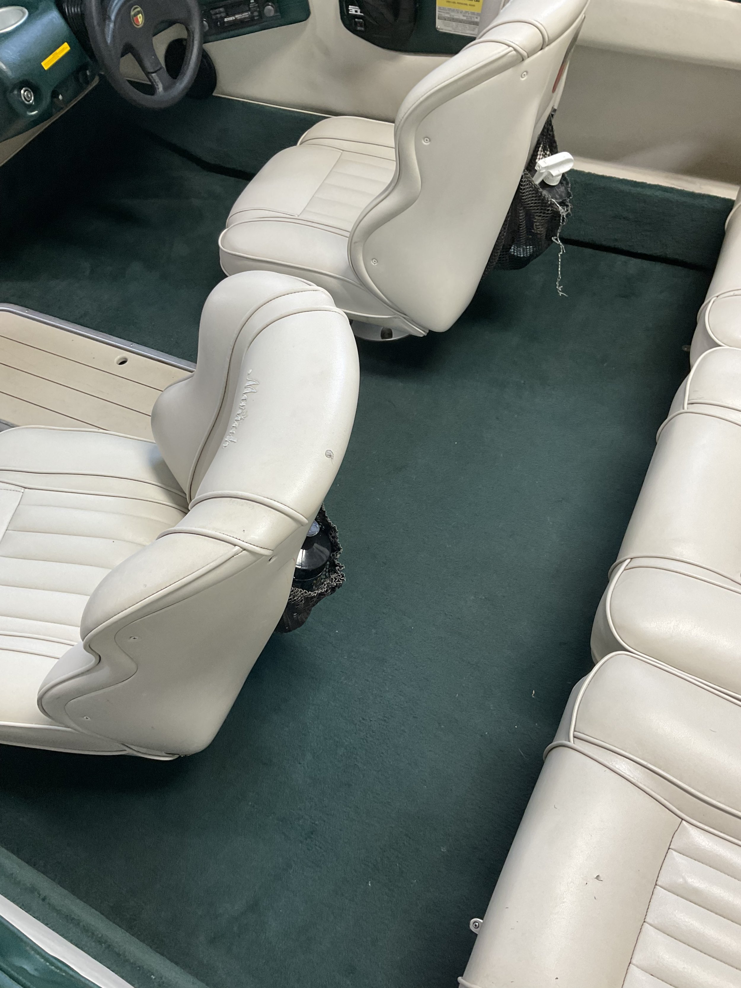 Interior of a boat with white leather seats and green carpeting.
