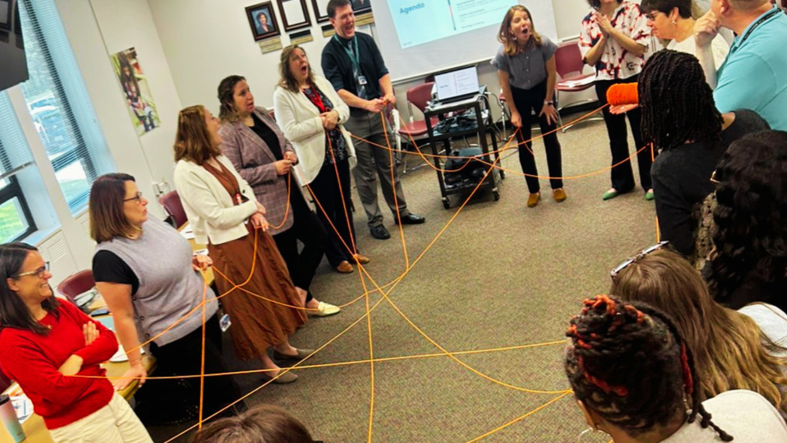 Facilitators and participants connected by an orange string web during a Due East planning exercise.