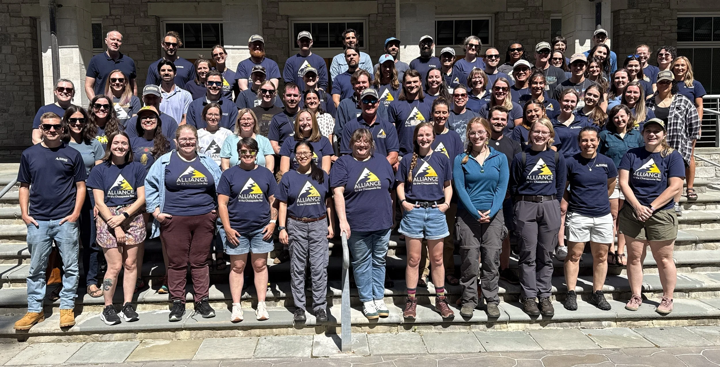Large group of Alliance for the Chesapeake Bay staff posing together on stone steps in matching navy shirts.