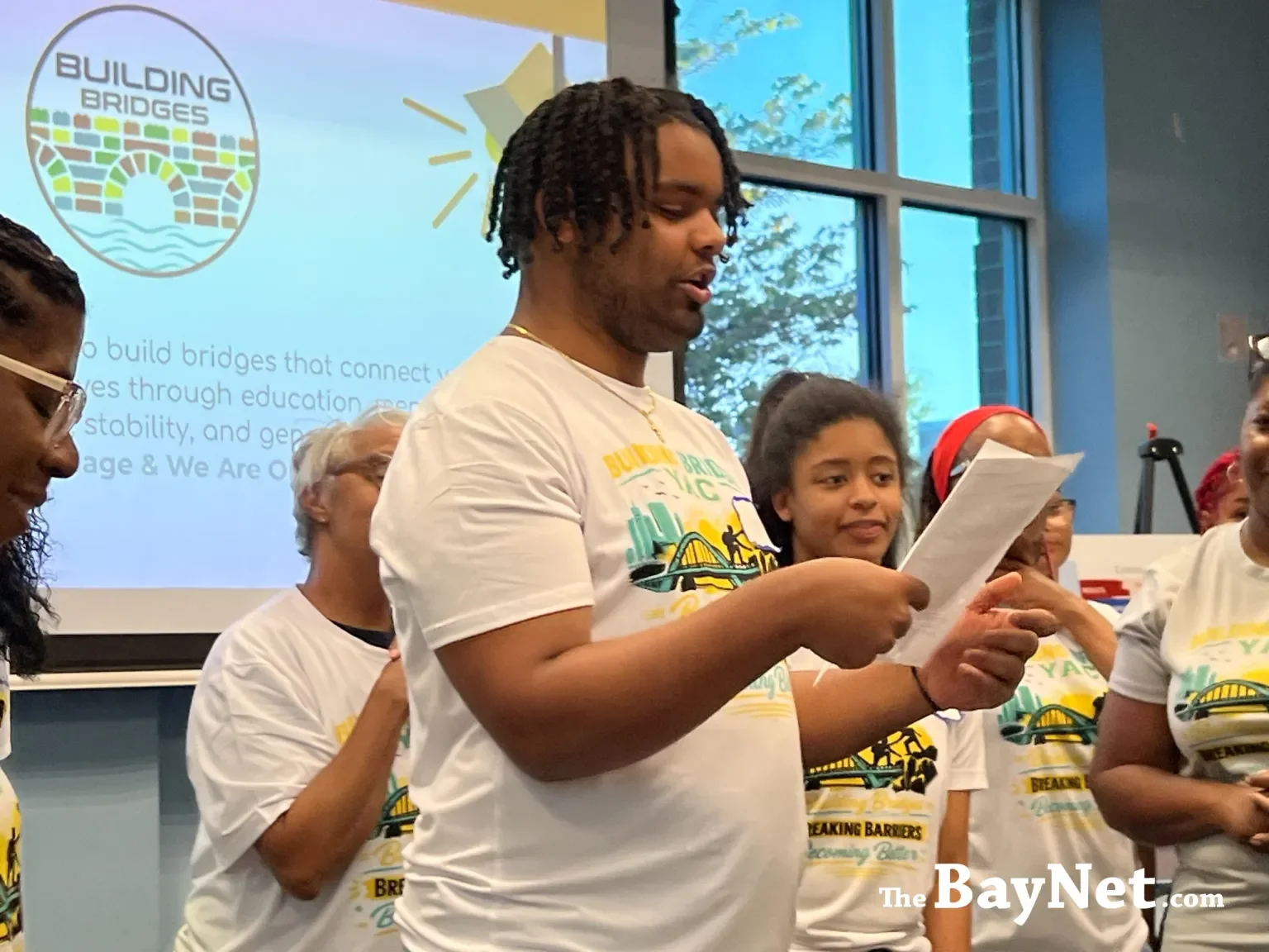 Young people in "Building Bridges" t-shirts present at a community strategy meeting, with a mission statement visible on the projection screen behind them.