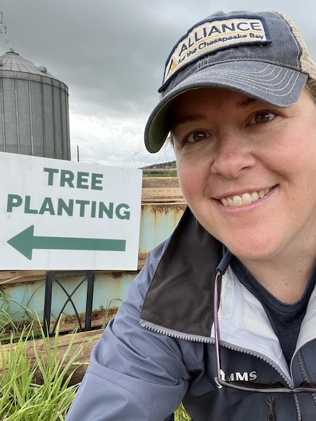 Kate Fritz taking a selfie beside a "Tree Planting" directional sign at a farm site.