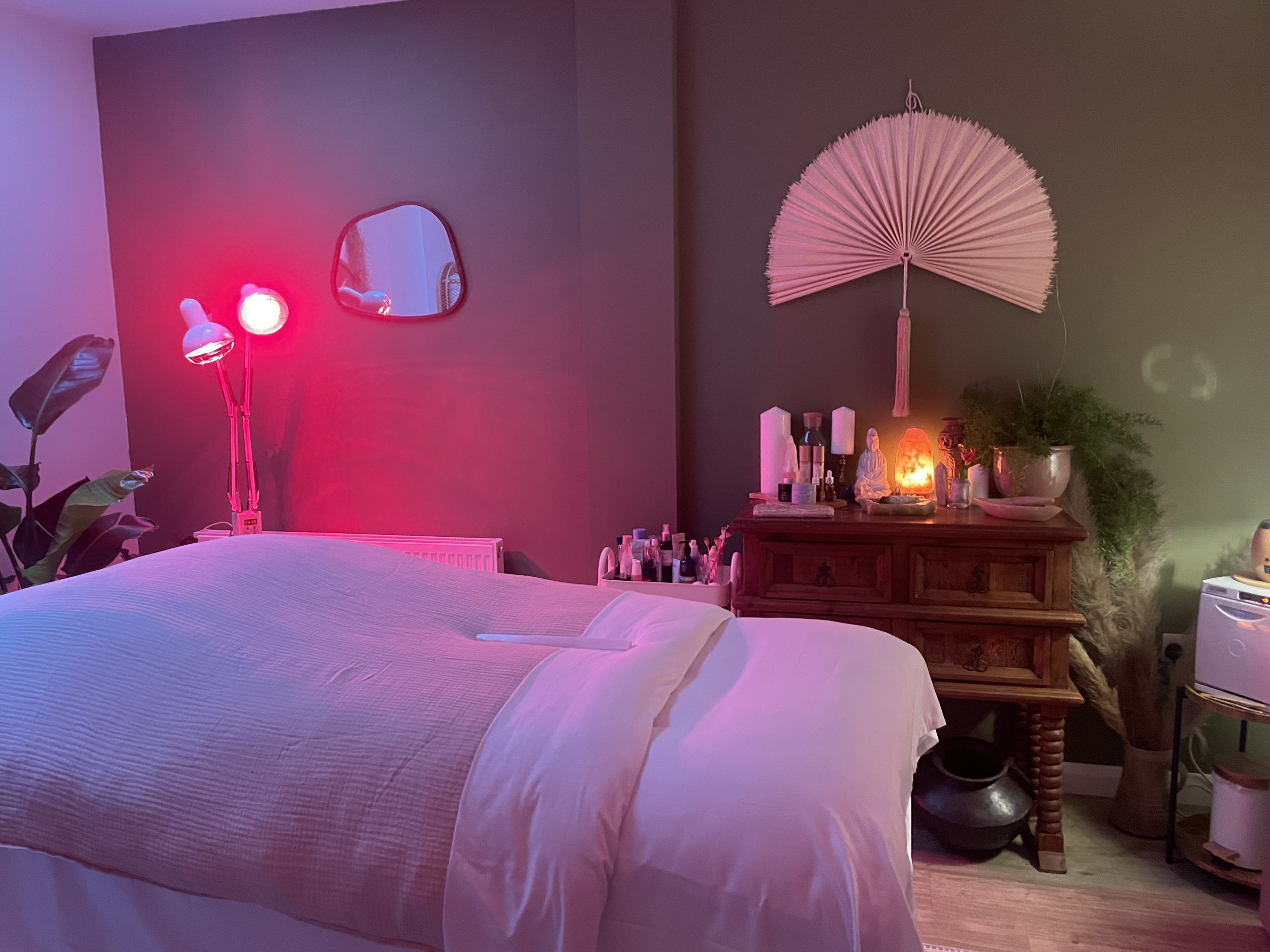 Person holding a colorful chakra pendulum over a person lying under a towel with a rose quartz crystal on their abdomen, in a calm and warm setting.