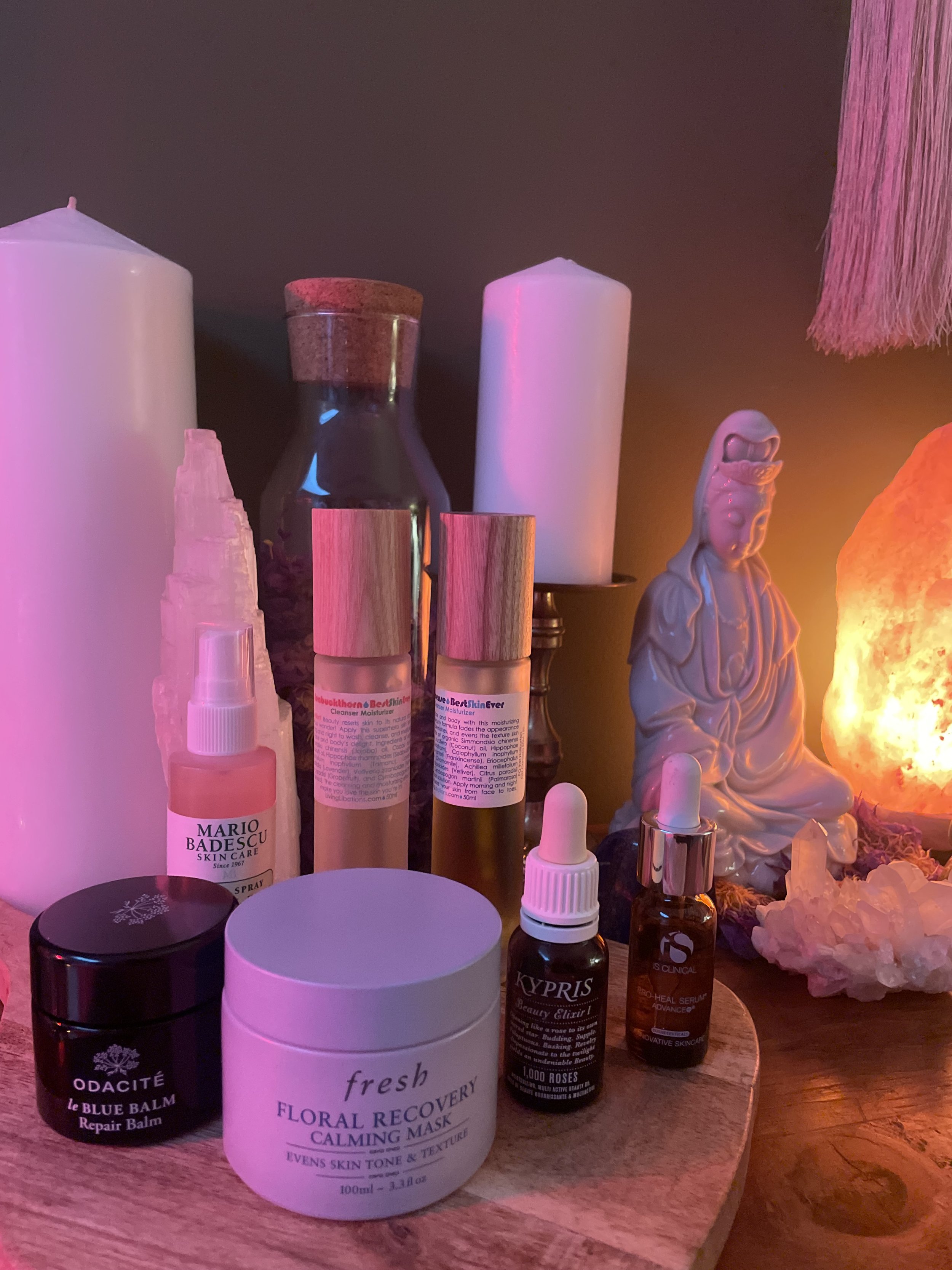 A white tray holding various skincare products, including bottles and tubes, placed on a white surface next to a lamp with a beige shade.