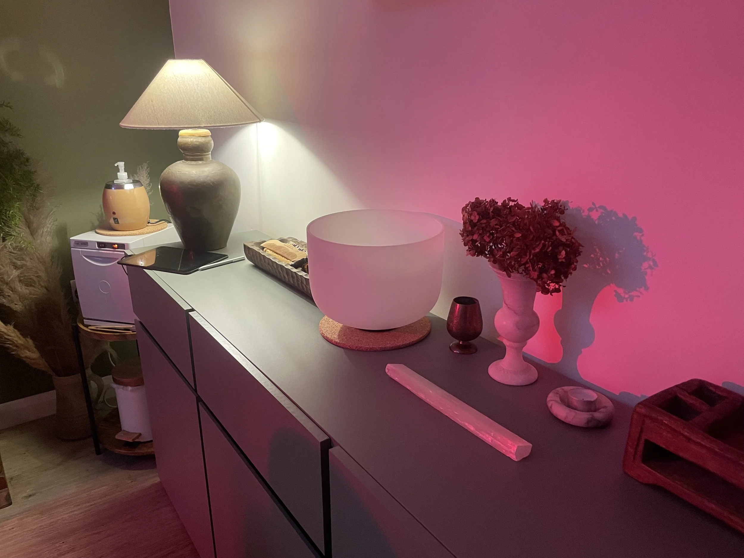 A white tray holding various skincare products, including bottles and tubes, placed on a white surface next to a lamp with a beige shade.