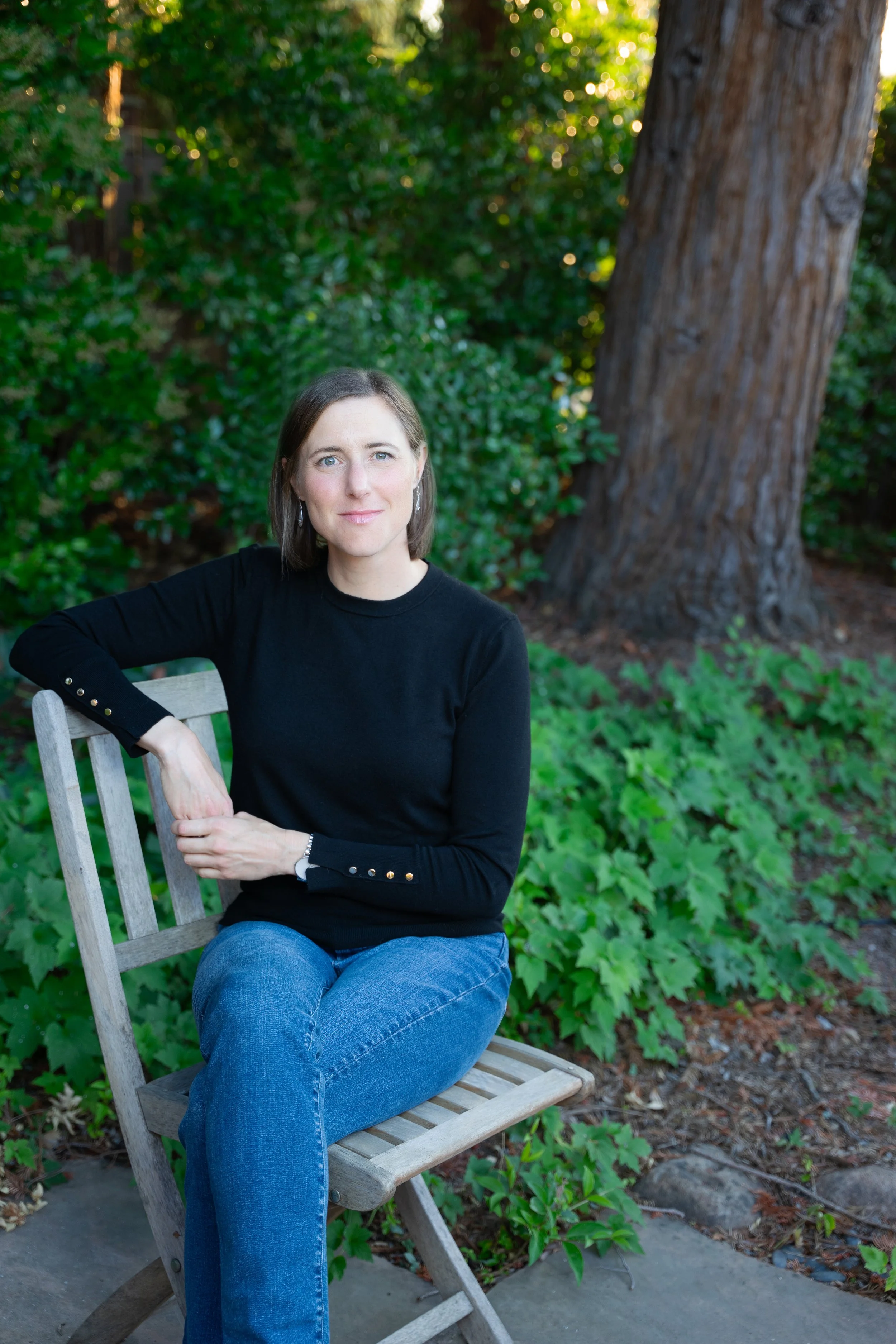 Crystal Herron sitting in a wood chair in front of a redwood tree