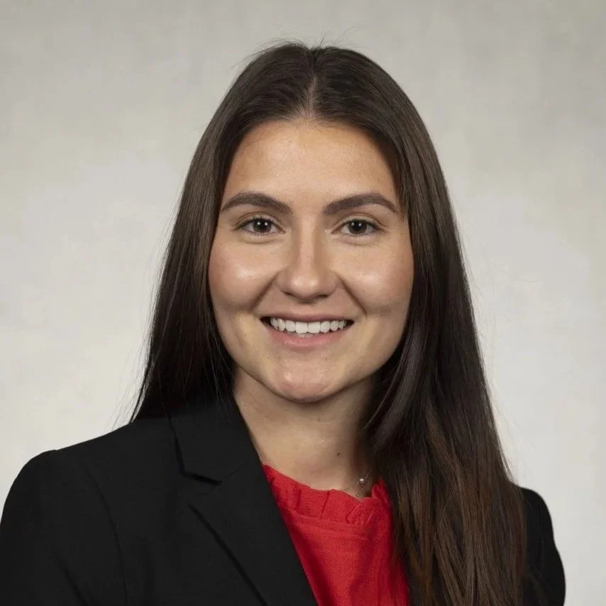 Woman with long dark brown hair wearing a red shirt and black blazer