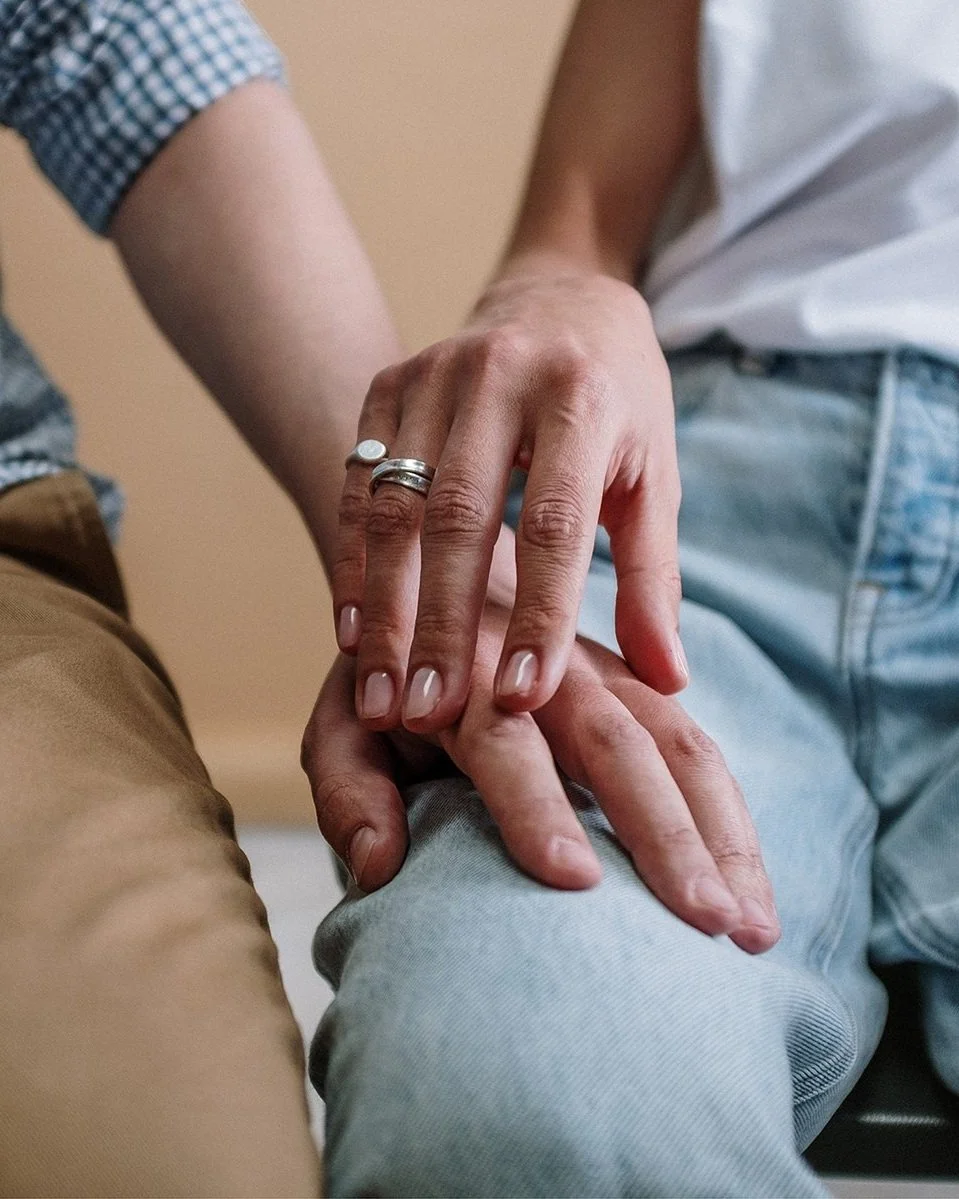 Close up of a couple's legs with their hands tentatively touching. They are in discernment counseling in Riverside CA to help them decide the future of their relationship. Should they divorce or work on it?