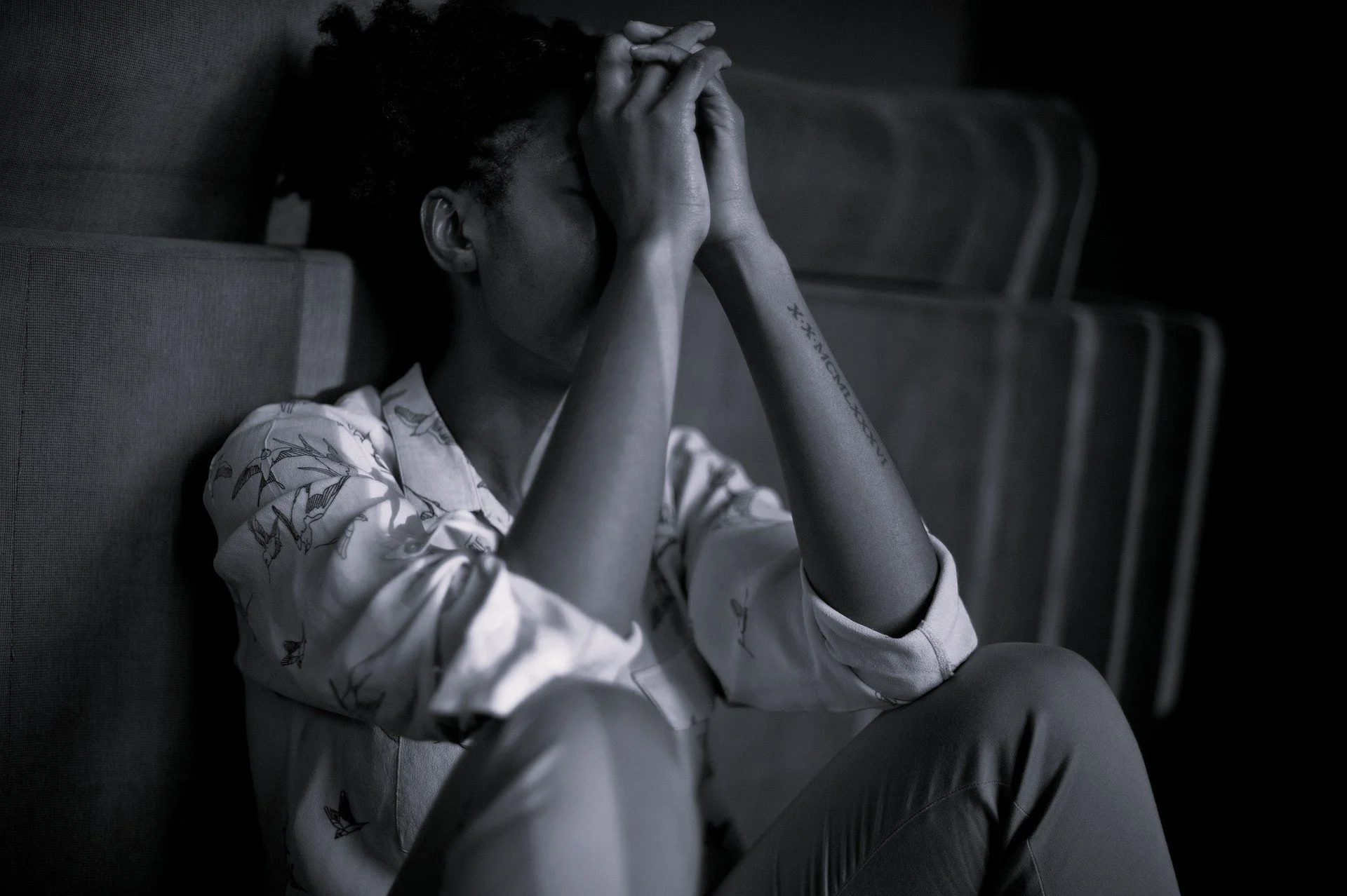 Black and whote photo of person with hands up covering face sad