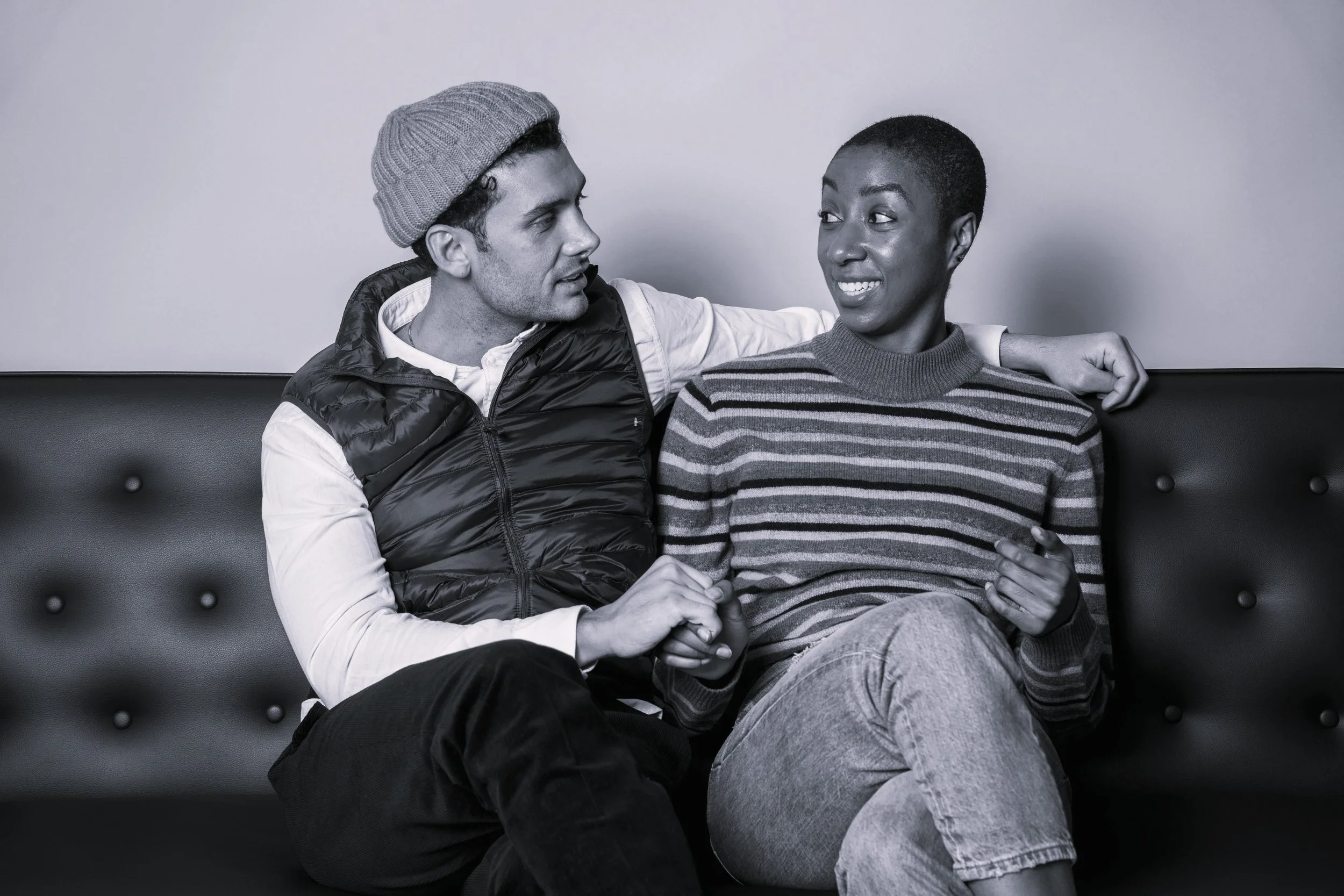 Black and White photo of couple holding handing looking at each other and sitting on a sofa