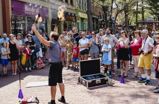 Street performer juggling fire on a busy sidewalk with spectators watching.