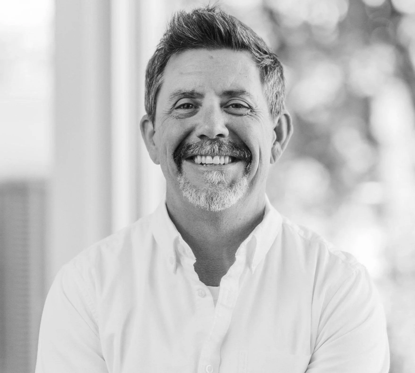 Black and white portrait of smiling middle-aged man with a beard and mustache, wearing a white collared shirt.