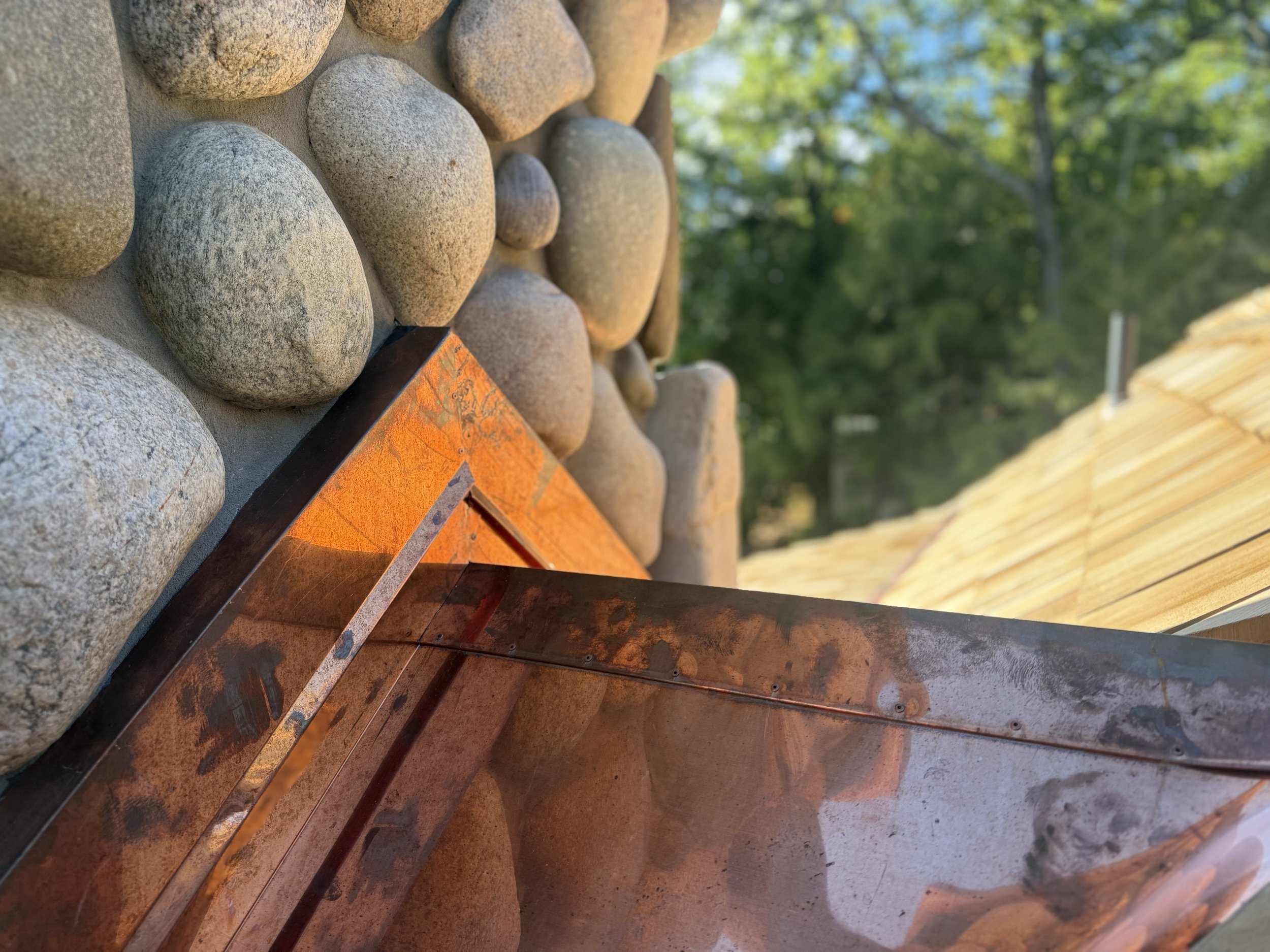 Copper cricket / saddle and counter flashing integrated into stone chimney on cedar shake roof overlooking Walloon Lake