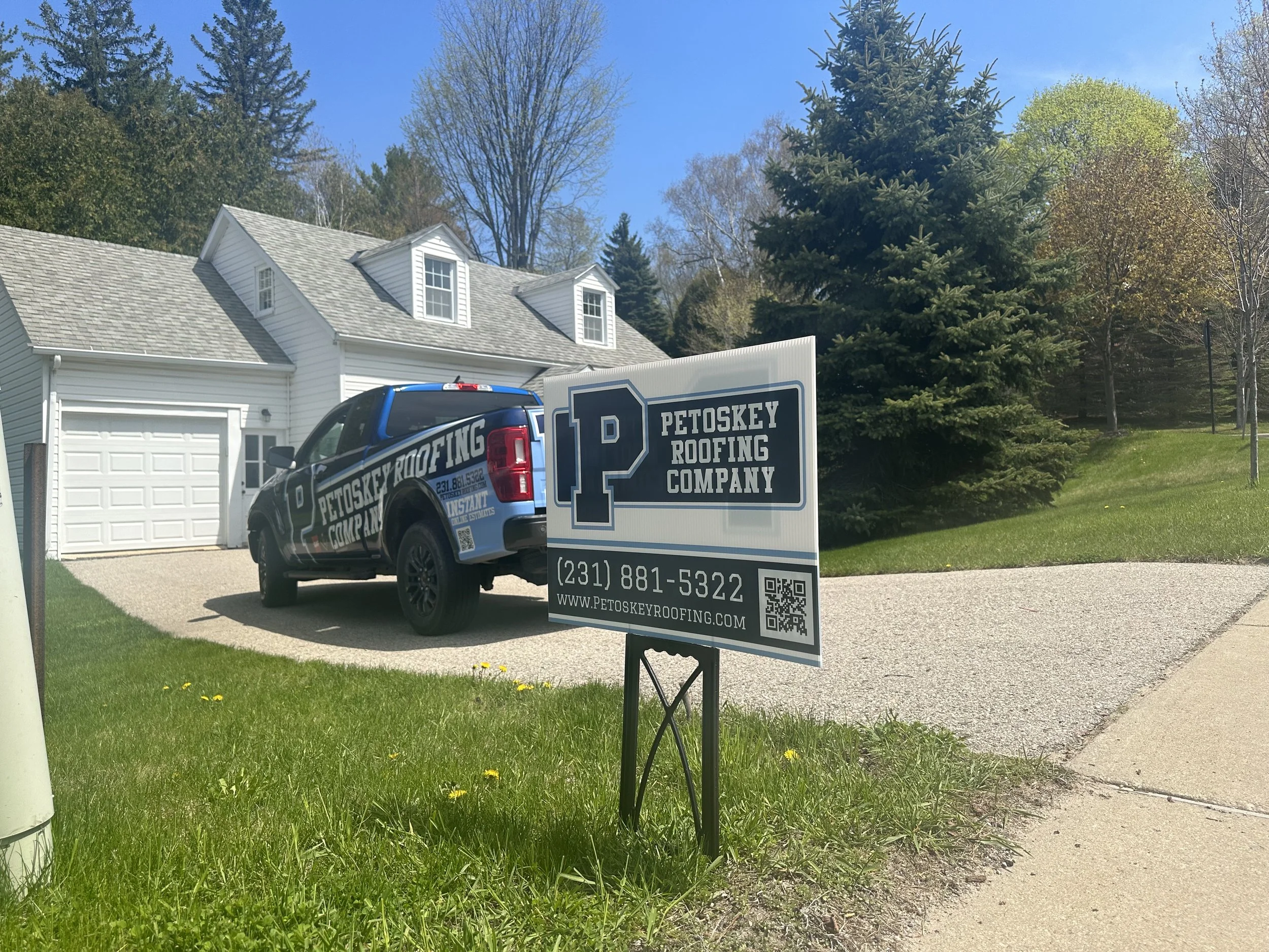 Petoskey Roofing Company truck and yard sign in front of a recently roofed white home in Petoskey, Michigan